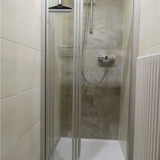 A modern shower with glass doors and a minimalist design. The room has bright tiled walls and is well-lit.