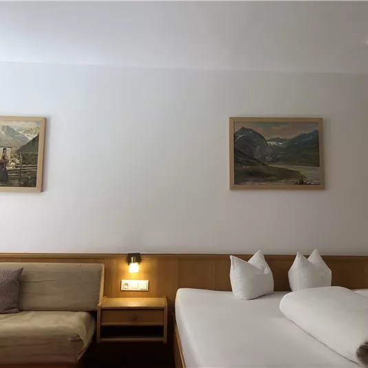 Ein gemütliches Zimmer mit einem Doppelbett und einer eleganten Couch. An den Wänden hängen zwei Landschaftsgemälde.