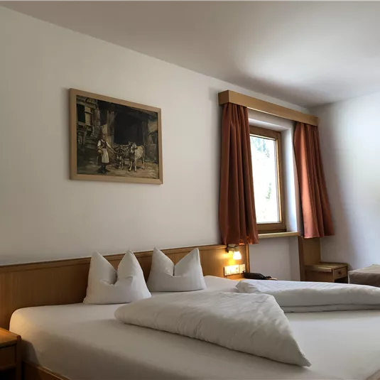 Ein gemütliches Schlafzimmer mit einem großen Bett und hellen Vorhängen. An der Wand hängt ein Gemälde, und es gibt eine Fenster mit natürlichem Licht.