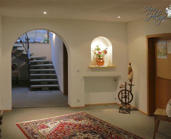 Ein einladender Flur mit einem Teppich und einem Treppenaufgang im Hintergrund. An der Wand befindet sich eine kleine Nische mit einer Blumenvase.