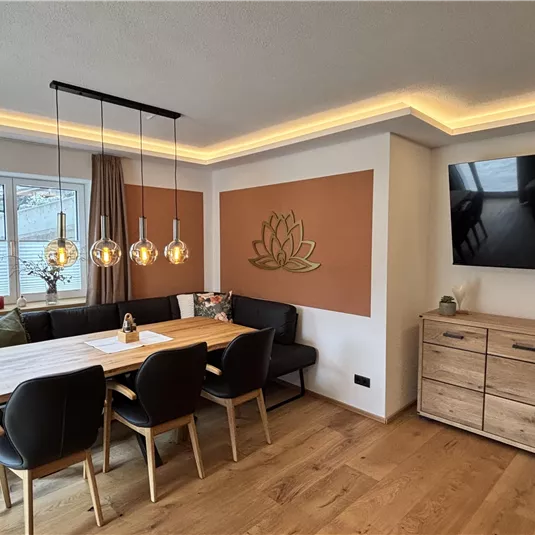 Ein modernes Esszimmer mit einem großen Tisch und eleganten Stühlen. Die warmen Lichter und die Holzverkleidung schaffen eine gemütliche Atmosphäre.