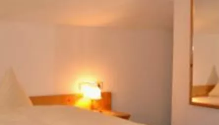 A cozy bedroom with a large bed and two pillows. In the background, there is a mirror and an adjoining bathroom.