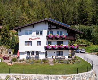 Ein charmantes Haus mit Blumenbalkonen in einer grünen Umgebung. Die friedliche Landschaft und die Berge im Hintergrund schaffen eine einladende Atmosphäre.