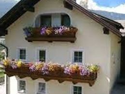 Ein charmantes Haus mit Balkonen, die mit bunten Blumen geschmückt sind. Im Hintergrund sind grüne Hügel und ein blauer Himmel zu sehen.