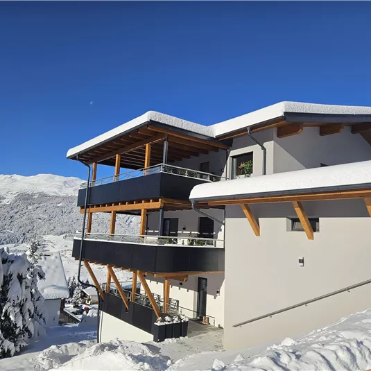 A modern building in a snow-covered landscape. The clear blue sky and the mountains in the background give the scene a wintry atmosphere.