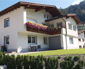 Ein modernes Haus mit einem schönen Balkon und bunten Blumen. Es hat einen großen Garten und eine malerische Berglandschaft im Hintergrund.