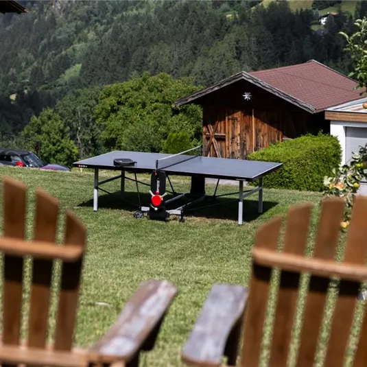 Ein schöner Garten mit einer Tischtennisplatte und Blick auf die Berge. Im Vordergrund stehen zwei Holzsessel.