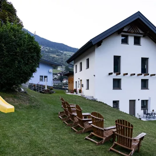 Ein modernes Haus in einer grünen Umgebung mit einem Spielplatz und einer Rutsche. Es gibt Gartenmöbel zum Entspannen im Freien.