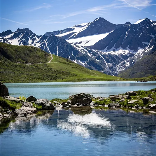 Ein klarer See spiegelt die schneebedeckten Berge wider. Der Himmel ist blau mit wenigen Wolken.