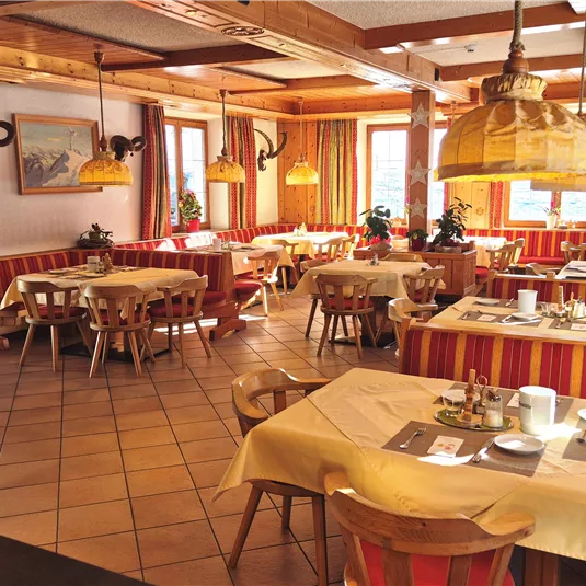 A cozy restaurant with wooden furniture and colorful curtains. The tables are elegantly set and provide an inviting atmosphere.