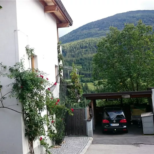 A picturesque residential area with a white building and a garage. In the background, green mountains and trees can be seen.