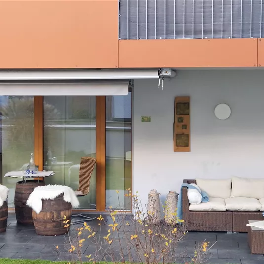 Ein moderner Außenbereich mit einer bequemen Couch und zwei Stühlen. Die Terrasse ist mit Fliesen und einem kleinen Tisch dekoriert.