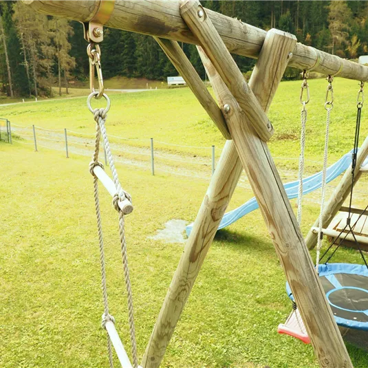 A playground with swings and a slide. The meadow is green and surrounded by trees.