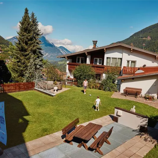 Eine ruhige Gartenlandschaft mit einem weiten Grasbereich und Blick auf die Berge. Es gibt mehrere Sitzmöglichkeiten und eine entspannte Atmosphäre.