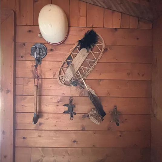 On a wooden wall hang various old objects, including a helmet, a snowshoe, and a tool. The atmosphere is rustic and traditional.