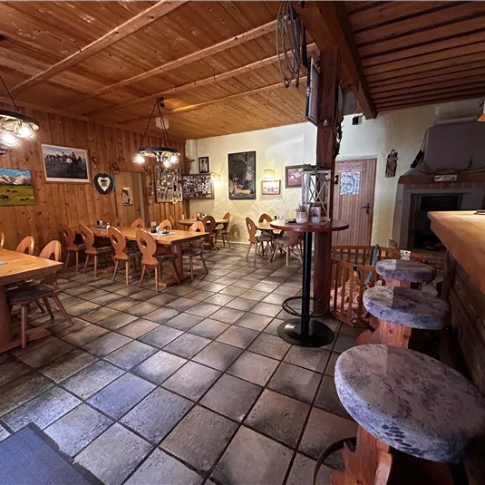 A cozy restaurant with wooden furniture and a warm, inviting atmosphere. The tables are neatly set, and there are pictures hanging on the walls.
