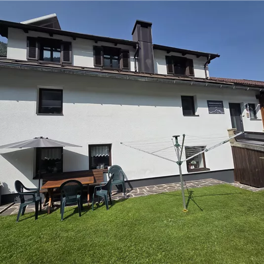 Ein weißes Haus mit einem grünen Rasen und einer Terrasse. Auf der Terrasse stehen Gartenmöbel und ein Wäscheständer.