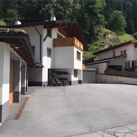 A quiet residential area with modern houses and a large square. Surrounded by green trees and mountains.