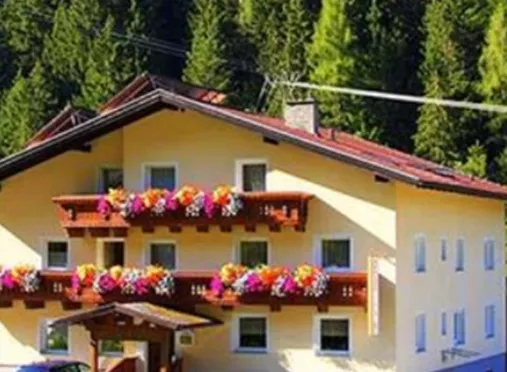 A beautiful house with colorful flower balconies surrounded by green trees. There are several cars in front of the building.