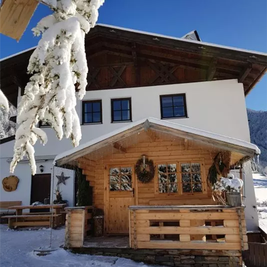 A beautiful wooden house in the snow with a cozy porch. The sky is clear and the surroundings look wintry and inviting.