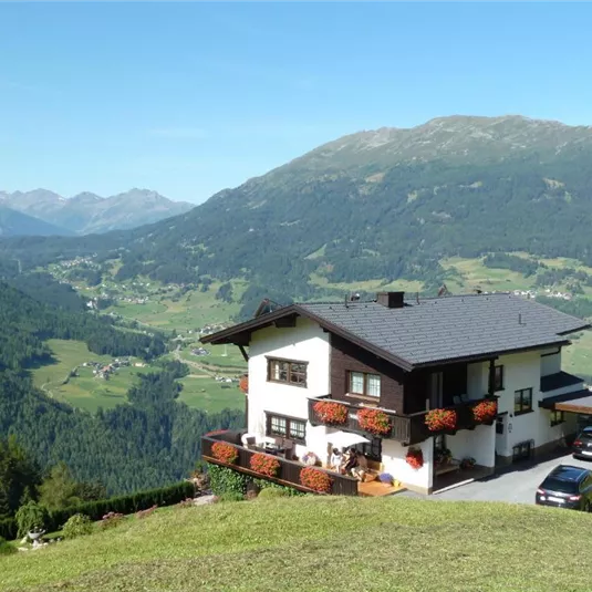 A cozy house in the mountains with blooming flower boxes. In the background, a beautiful landscape of mountains and valleys unfolds.