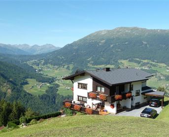 A cozy house in the mountains with blooming flower boxes. In the background, a beautiful landscape of mountains and valleys unfolds.