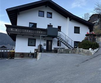 Ein modernes Haus mit weißer Fassade und einem Balkon. Es steht an einer kleinen Straße und ist von einer malerischen Landschaft umgeben.