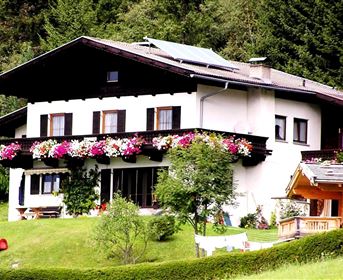 Ein schönes Haus mit einem Balkon voller Blumen. Der Garten ist grün und ein Spielplatz ist sichtbar.