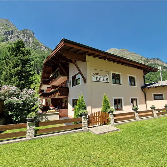 A cozy house in the mountains with a green garden. Surrounded by trees and a beautiful mountain backdrop.