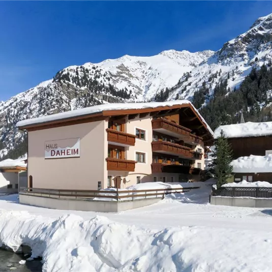A cozy house in the winter mountains, surrounded by snow-covered peaks. Clear blue skies and serene nature create a peaceful atmosphere.