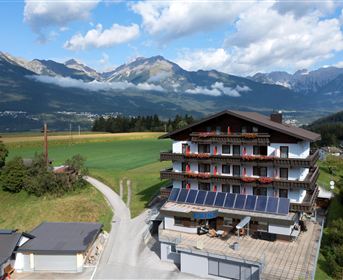 Ein malerisches Hotel in den Bergen mit einer schönen Aussicht auf die Landschaft. Die Umgebung ist grün und bewaldet, umgeben von majestätischen Bergen und einem klaren Himmel.