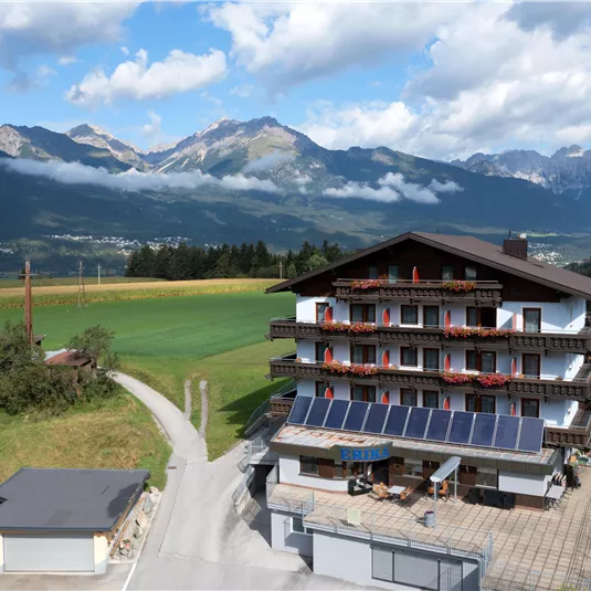 A picturesque hotel in the mountains with a beautiful view of the countryside. The surroundings are green and wooded, surrounded by majestic mountains and a clear sky.