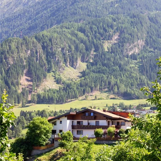 A picturesque house amidst green fruit trees, surrounded by high mountains. The idyllic landscape displays a tranquil atmosphere in nature.