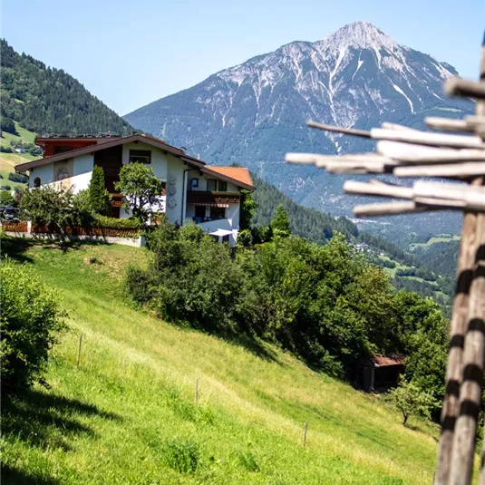A beautiful house in a green landscape with mountains in the background. The sky is clear and sunny.