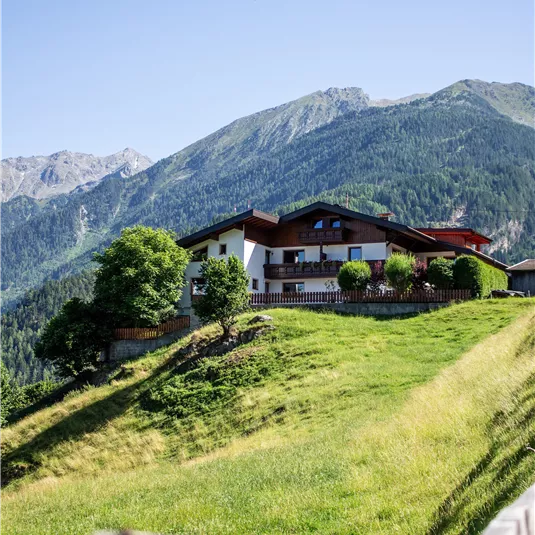 A beautiful house on a hill, surrounded by green meadows and mountains. The sky is blue and clear.