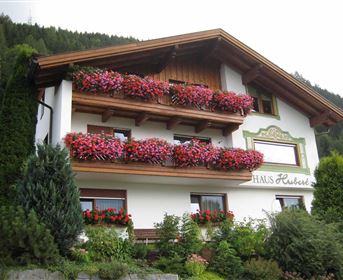 A charming house with colorful flower boxes on the balconies.  
Surrounded by green trees and mountains.