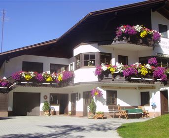 Ein traditionelles Gebäude mit einem schönen Balkon, geschmückt mit bunten Blumen. Die Umgebung ist sonnig und einladend.