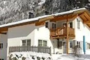 A cozy house in the snow with mountains in the background. The landscape is wintry and peaceful.