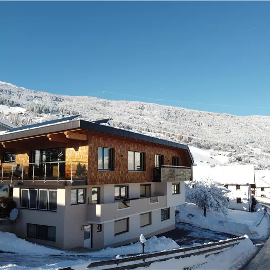 A snow-covered building in a beautiful winter landscape. The surrounding mountains are also covered with snow and the sky is bright blue.