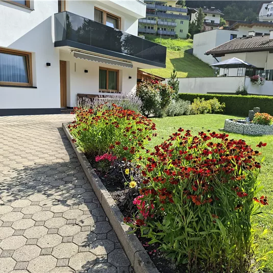 Ein schöner Garten mit bunten Blumen vor einem modernen Haus. Es gibt eine gepflasterte Auffahrt und eine gepflegte Rasenfläche.