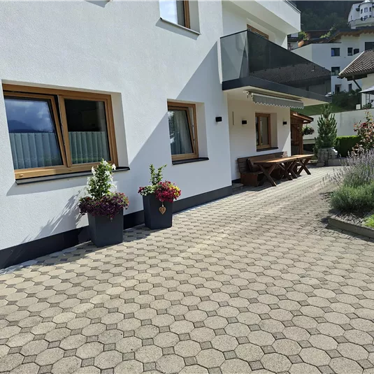 Ein modernes Haus mit hellen Wänden und einer Terrasse. Der Außenbereich ist mit Blumen und Gras angelegt.