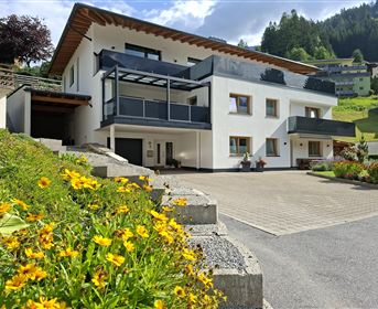 A modern house with a balcony in a beautiful landscape.  
Colorful flowers adorn the entrance area.