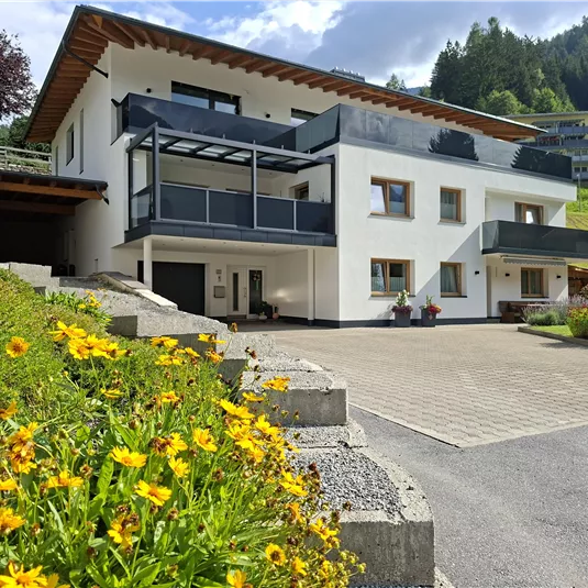 Ein modernes Haus mit Balkon in einer schönen Landschaft. Bunte Blumen schmücken den Eingangsbereich.