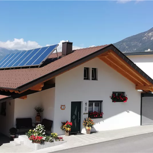A modern house with solar panels on the roof. The entrance area is decorated with colorful flowers and there is a beautiful mountain landscape in the background.