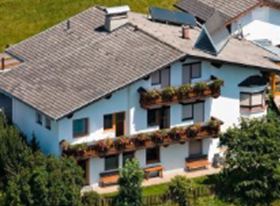 Ein hübsches Haus mit mehreren Balkonen und einem Garten. Umgeben von grüner Wiese und Bäumen.