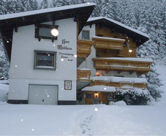 A cozy house in winter, covered with snow. The sky is gray and snowflakes are falling.