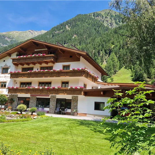 A cozy Alpine house surrounded by green meadows and mountains. The outdoor area is designed with colorful flowers and a well-kept garden.