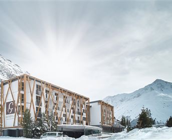 A modern hotel amidst snowy mountains. The sun shines behind the mountains.