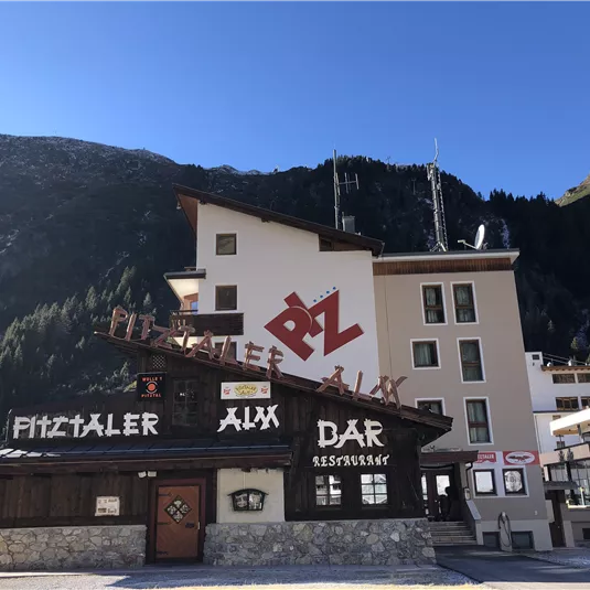 Ein Gebäude mit traditioneller Architektur inmitten von Bergen. Die Fassade zeigt eine auffällige Beschilderung für eine Bar und ein Restaurant.