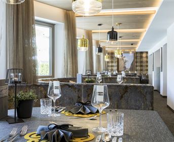 Ein elegantes Restaurant mit modernen Möbeln und stilvoll gedeckten Tischen. Große Fenster sorgen für viel Tageslicht und schaffen eine einladende Atmosphäre.